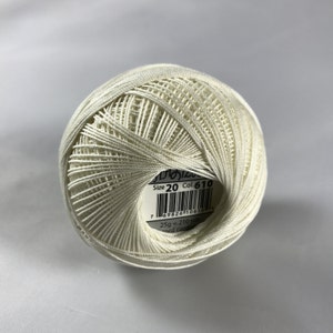 May include: A white ball of size 20 cotton thread with a label that reads "Size 20 Col. 610" and a barcode. The label also states "25g = 210 yds cord coton."