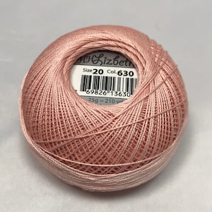 Puede incluir: Una madeja de hilo de bordar rosa pálido, tamaño 20, color 630, con una etiqueta que dice "Lizbeth" y "69826 13630 25g = 210 yd".