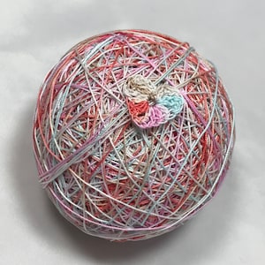 May include: A spherical ball of yarn in pastel colors, including pink, peach, and light blue, with a small, crocheted flower in the center. The yarn is intricately woven, creating a textured surface. This craft item is suitable for knitting or crochet projects.