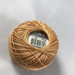 Puede incluir: Una madeja de hilo de bordar beige con una etiqueta que dice "Lizbeth Tamaño 20 Col. 715".