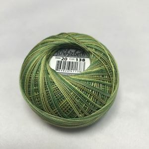 以下が含まれることがあります： DMC Lizbeth Size 20 Col. 138とラベルが付いた、緑と茶色の刺繍糸のボールです。