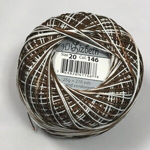 Puede incluir: Una madeja de hilo de bordar marrón y blanco con una etiqueta que dice "Lizbeth Tamaño 20 Col. 146 25g = 210 yds Cord cordonnet"