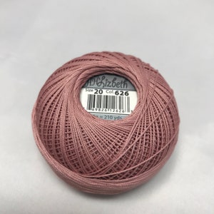 Puede incluir: Una madeja de hilo de bordar rosa de tamaño 20 con una etiqueta que dice "Lizbeth" Tamaño 20 Col. 626 y un código de barras. La etiqueta también dice "210 yds".