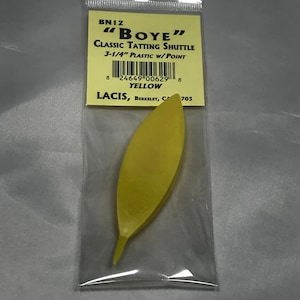 Puede incluir: Una lanzadera de tatting de plástico amarillo etiquetada como "BOYE" Classic Tatting Shuttle 3-1/4" Plastic w/Point. La lanzadera está empaquetada en una bolsa de plástico transparente con una etiqueta amarilla que también incluye el nombre de la marca "LACIS" y la ubicación "BERKELEY, CA 703".