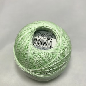 May include: A ball of light green crochet thread. The label reads "Lizbeth Size 20 Col. 187". The thread is tightly wound, showing the texture of the yarn. The ball contains approximately 210 yards of thread.