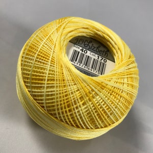 Puede incluir: Una madeja de hilo de bordar amarillo con una etiqueta blanca que dice "HH Sizbeth Size 40 Col. 170" y un código de barras.