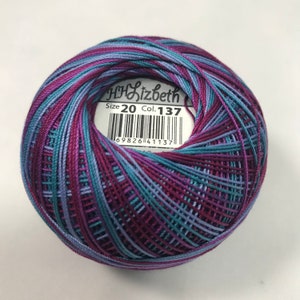 Può includere: Un gomitolo di filo da ricamo multicolore in tonalità di viola, blu e turchese. Il gomitolo ha un'etichetta che recita "HHLizbeth Taglia 20 Col. 137" e un codice a barre.