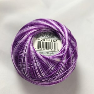 Op de afbeelding: Een bol paarse en witte borduurgaren met een label met de tekst "Size 20 Col. 162" en "25g = 210 yds".