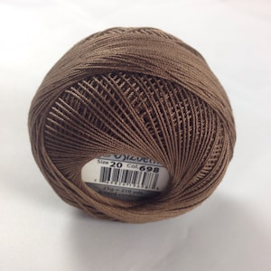 Può includere: Un gomitolo di filo da ricamo marrone con un'etichetta bianca che recita "Size 20 Col. 698 25g = 210 yds cord.com"
