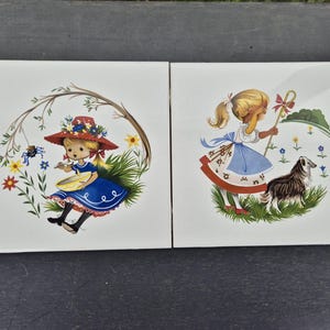 Può includere: Due piastrelle quadrate in ceramica con illustrazioni vintage. Una piastrella raffigura una ragazza con un vestito blu e un cappello rosso con un ragno e fiori. L'altra mostra una ragazza con un cane in un campo. Entrambe le piastrelle hanno uno sfondo bianco.