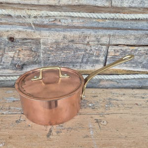 Könnte beinhalten: Ein Set aus drei Keramikbechern mit gesprenkelter, matter Oberfläche. Die Becher sind in Creme-, Hellgrau- und Dunkelgrautönen gehalten. Jeder Becher hat ein schlichtes, minimalistisches Design und einen abgerundeten Henkel.