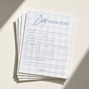 May include: A stack of rectangular paper cards featuring a light blue and white gingham pattern. The text reads Baby PREDICTIONS with fields for name, gender, weight, height, hair color, eye color, a calendar grid for date and time, and advice.