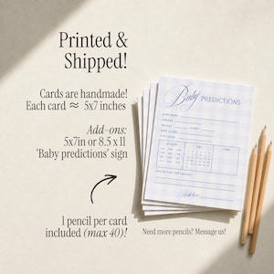 May include: A stack of light blue and white gingham patterned baby prediction cards with text fields for name, gender, weight, height, hair and eye color, and a calendar section. Three wooden pencils are placed next to the cards on the surface.