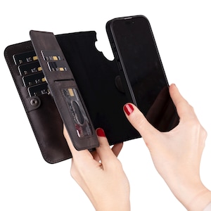 May include: A dark brown leather phone case with card slots and a black phone. The case is open, revealing multiple card slots and a clear ID window. The phone is black and fits snugly into the case.