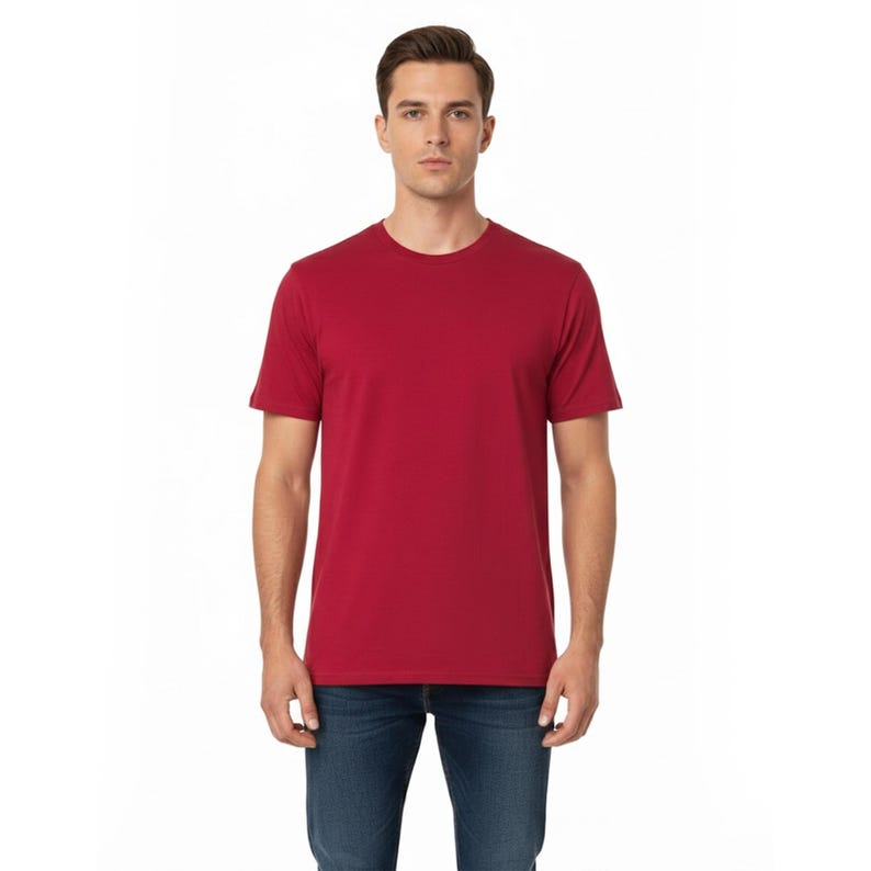 May include: A solid red crew neck t-shirt. The short-sleeved shirt is made of a soft material and is being worn with blue jeans. The model is standing in front of a white background.