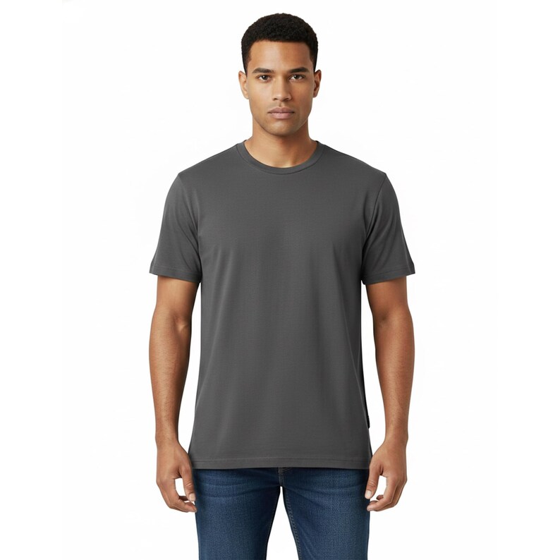 May include: A charcoal gray crew neck t-shirt. The short-sleeved shirt is made of a soft material and is being worn with blue jeans. The model is standing in front of a white background.