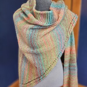 Peut inclure: Un châle triangulaire tricoté à la main présentant un motif de fil panaché aux teintes mélangées de vert tendre, pêche, bleu clair et beige. Le vêtement affiche une texture en point mousse uniforme avec une bordure à œillets décorative.
