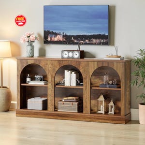 May include: A wooden entertainment center with three arched storage spaces. The center has a TV on top, a speaker, and decorative items like books, lanterns, and a vase of flowers. The wood has a rustic, distressed finish.