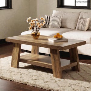 May include: A rectangular wooden coffee table with a lower shelf. The table has a natural wood grain finish and sturdy, angled legs. A glass vase with flowers, a bowl of oranges, and a book are on the table. The table sits on a cream-colored rug.