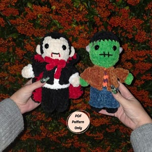 May include: Two handmade crochet Halloween dolls: a vampire with a black cape and red bow tie, and a Frankenstein's monster with green skin and a brown jacket. The dolls are held against a backdrop of orange berries. The text "PDF Pattern Only" is visible.