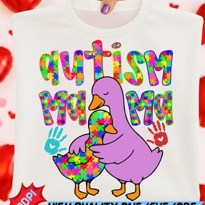Puede incluir: Camiseta blanca con las palabras "Autism Mom" en letras de rompecabezas de colores. También se representan dos patos de dibujos animados, uno abrazando al otro. El diseño incluye huellas de manos y el texto "HIGH QUALITY PNG/SVG/PDF DESIGN".