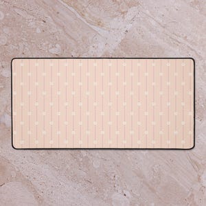 May include: A rectangular desk mat with a black border. The mat features a light peach background with vertical dotted lines and small white flower designs. The overall design is simple and elegant.
