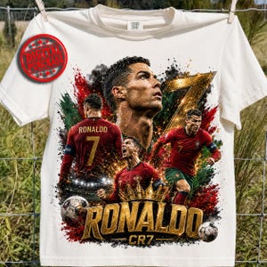 Outdoor white t-shirt mockup hanging on a fence, featuring a bold Ronaldo CR7 football design with multiple action poses, a large portrait, gold number 7, crown, soccer balls, red and green paint splashes, black smoky grunge texture, and metallic gold “RONALDO” text. Red Digital Purchase stamp shows this is a printable digital PNG download.