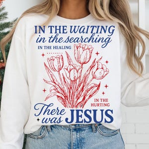 May include: White sweatshirt featuring a red and blue floral design with the words "IN THE WAITING, IN THE SEARCHING, IN THE HEALING, IN THE HURTING, There was JESUS."