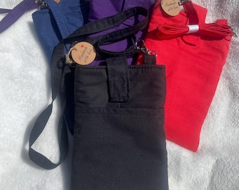Puede incluir: Una colección de cuatro bolsos bandolera rectangulares en negro, rojo, morado y azul. Cada bolso cuenta con un cierre de solapa vertical, una correa de tela ajustable a juego con clips de metal y una pequeña etiqueta circular con la frase Handmade with love.