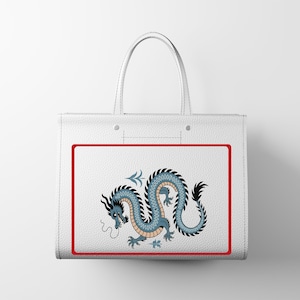 Puede incluir: Bolso tote blanco con un dise&ntilde;o de drag&oacute;n azul y negro dentro de un borde rojo. El drag&oacute;n tiene un cuerpo largo y sinuoso. El bolso tiene dos asas blancas. El bolso es de material texturizado.