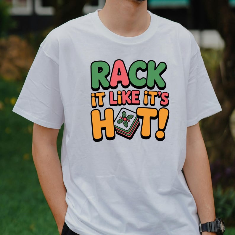 May include: White t-shirt with the text "RACK IT LIKE IT'S HOT!" in green, pink, and orange. The design includes a graphic of a stack of food with a flower on top. The shirt is a casual style.