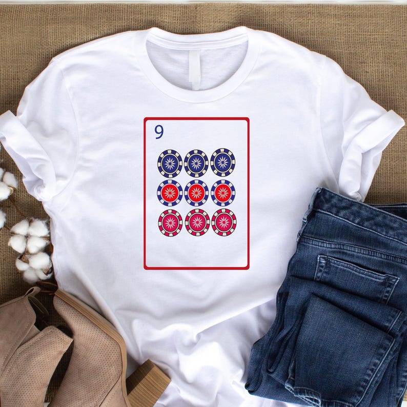 Puede incluir: Camiseta blanca con un dise&ntilde;o de carta de juego. La carta muestra el n&uacute;mero 9 y nueve s&iacute;mbolos tipo fichas de p&oacute;quer en una cuadr&iacute;cula de 3x3. Las fichas son azules, rojas y rosas.