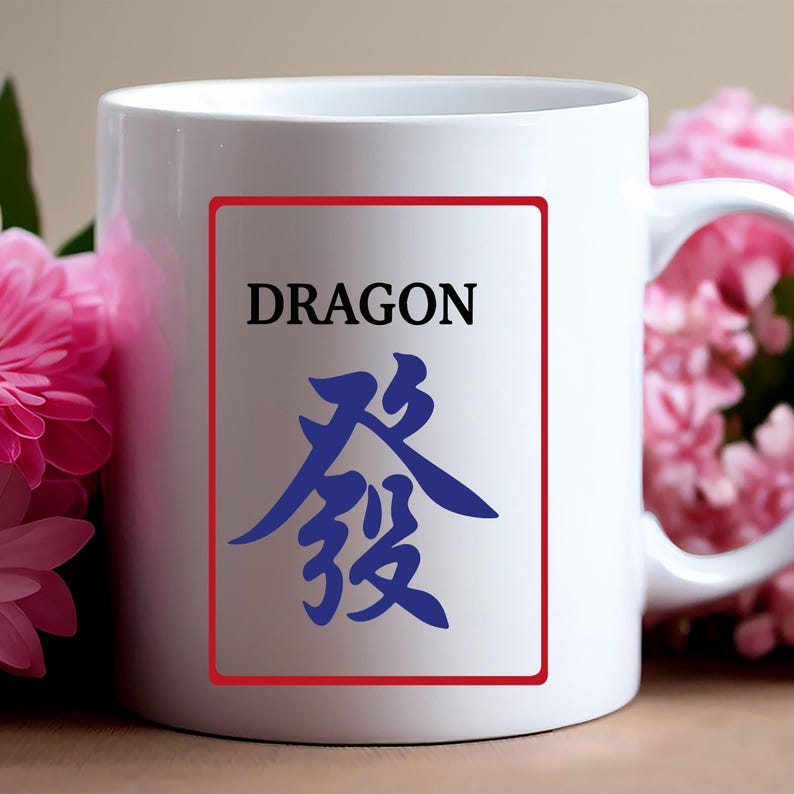 Puede incluir: Taza de cer&aacute;mica blanca con un rect&aacute;ngulo con borde rojo con la palabra "DRAGON" encima de un car&aacute;cter chino azul. La taza tiene un asa blanca y est&aacute; sobre un fondo con flores rosas.