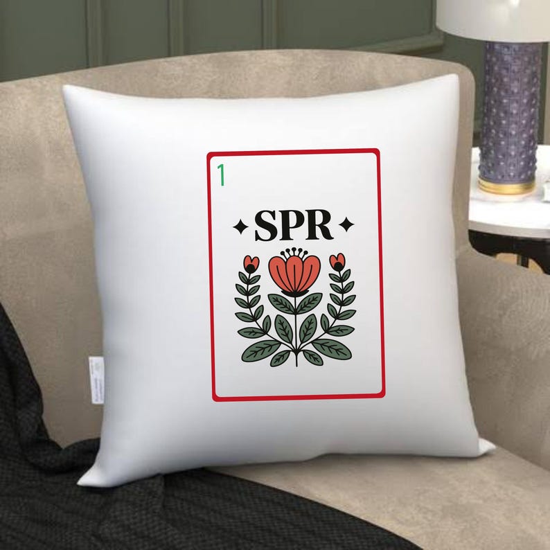 Puede incluir: Coj&iacute;n cuadrado blanco con borde rojo. El dise&ntilde;o presenta un motivo floral y la palabra "SPR". El dise&ntilde;o incluye una flor roja, hojas verdes y el n&uacute;mero "1" en la esquina superior izquierda.