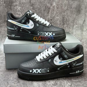 May include: Pair of black sneakers with white laces and a white Nike swoosh. The shoes have custom designs in white, yellow, green, and blue. The word "AIR" is printed on the side of the sole.