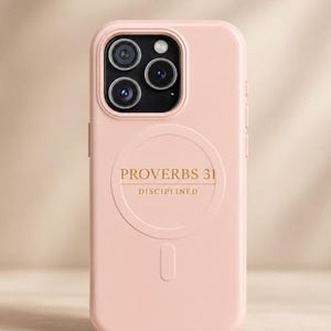 May include: A light pink smartphone case featuring a triple-lens camera cutout at the top. The back of the case displays a circular MagSafe-style ring with the gold-colored text PROVERBS 31 and the word DISCIPLINED printed directly underneath.