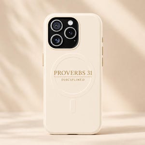 Peut inclure: Une coque de smartphone couleur crème avec un anneau d'alignement MagSafe circulaire et le texte PROVERBS 31 DISCIPLINED imprimé en doré. La coque présente une découpe pour un système de triple objectif et une encoche verticale en bas.