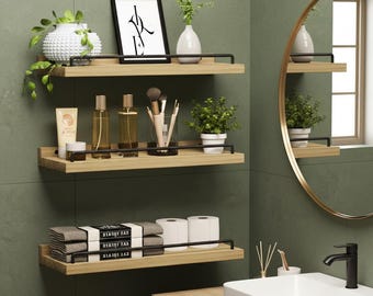 May include: Three wooden floating shelves with black metal railings are mounted on a green wall. The shelves hold decorative items like plants, vases, framed art, and toiletries. A round mirror and a white sink are also visible.