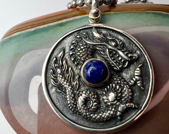 May include: Silver pendant featuring a detailed dragon design with a blue lapis lazuli stone in the center.