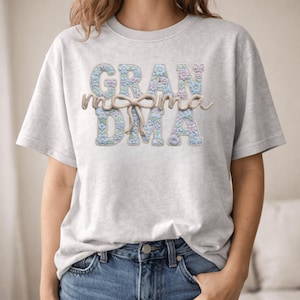 Peut inclure: Un t-shirt gris clair avec le mot "GRANDMA" dans un motif floral. Le mot "momma" est écrit dans une police de caractères en forme de corde, noué avec un nœud. Le t-shirt est fait d'une matière douce.