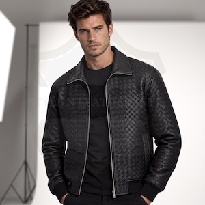 May include: A black jacket featuring a woven leather texture, a classic collar, and a silver-toned front zip closure. The garment includes ribbed cuffs and a ribbed hem, providing a structured fit. The design is consistent throughout the body.
