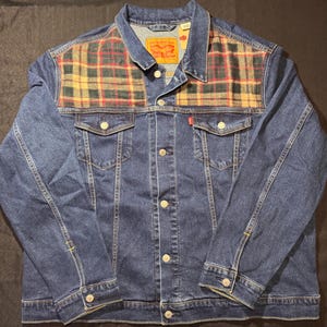 May include: A blue denim jacket with a plaid pattern across the shoulders. The jacket has a button-up front, two chest pockets, and two side pockets. A red Levi's tag is visible on the chest.