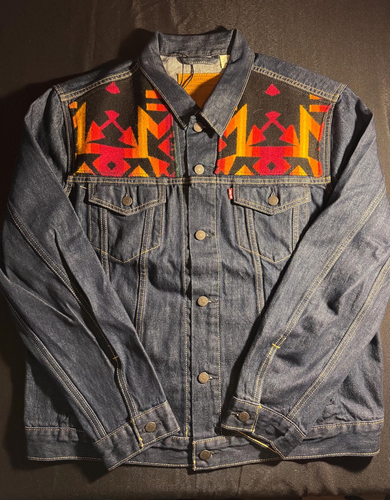 Puede incluir: Chaqueta vaquera azul oscuro con un dise&ntilde;o geom&eacute;trico colorido en la pechera. El dise&ntilde;o presenta formas rojas, naranjas y amarillas sobre un fondo negro. La chaqueta tiene cierres de bot&oacute;n, bolsillos y un cuello cl&aacute;sico.