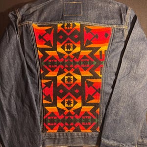 Puede incluir: Chaqueta vaquera con un panel trasero con estampado geom&eacute;trico vibrante. El patr&oacute;n presenta formas rojas, naranjas, amarillas y negras. La chaqueta tiene un cuello cl&aacute;sico, cierres de bot&oacute;n y dos bolsillos delanteros.