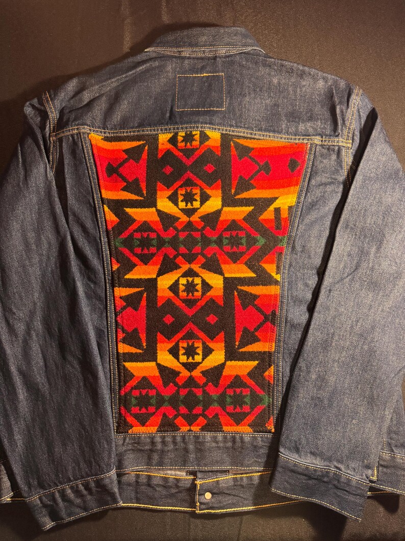 Puede incluir: Chaqueta vaquera con un panel trasero con estampado geom&eacute;trico vibrante. El patr&oacute;n presenta formas rojas, naranjas, amarillas y negras. La chaqueta tiene un cuello cl&aacute;sico, cierres de bot&oacute;n y dos bolsillos delanteros.