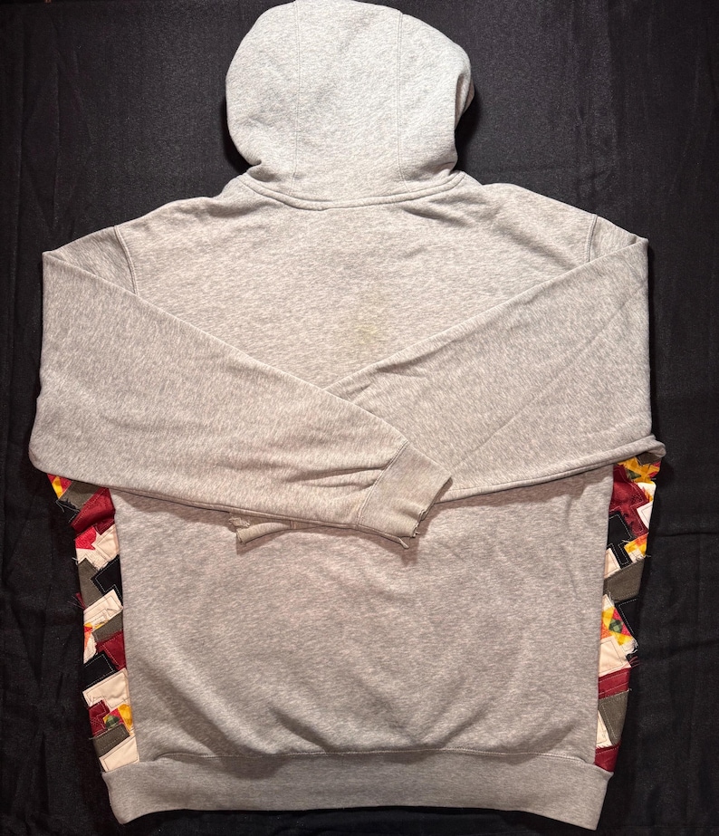 May include: A gray hoodie with a hood and long sleeves. The back of the hoodie features a colorful patchwork design along the lower sides. The hoodie is made of a soft, comfortable material.