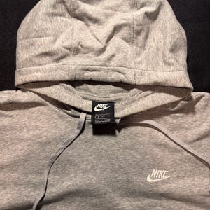 May include: A gray Nike hoodie with a drawstring and a hood. The Nike logo is visible on the chest and on a tag near the neckline. The hoodie is made of a soft, comfortable material.