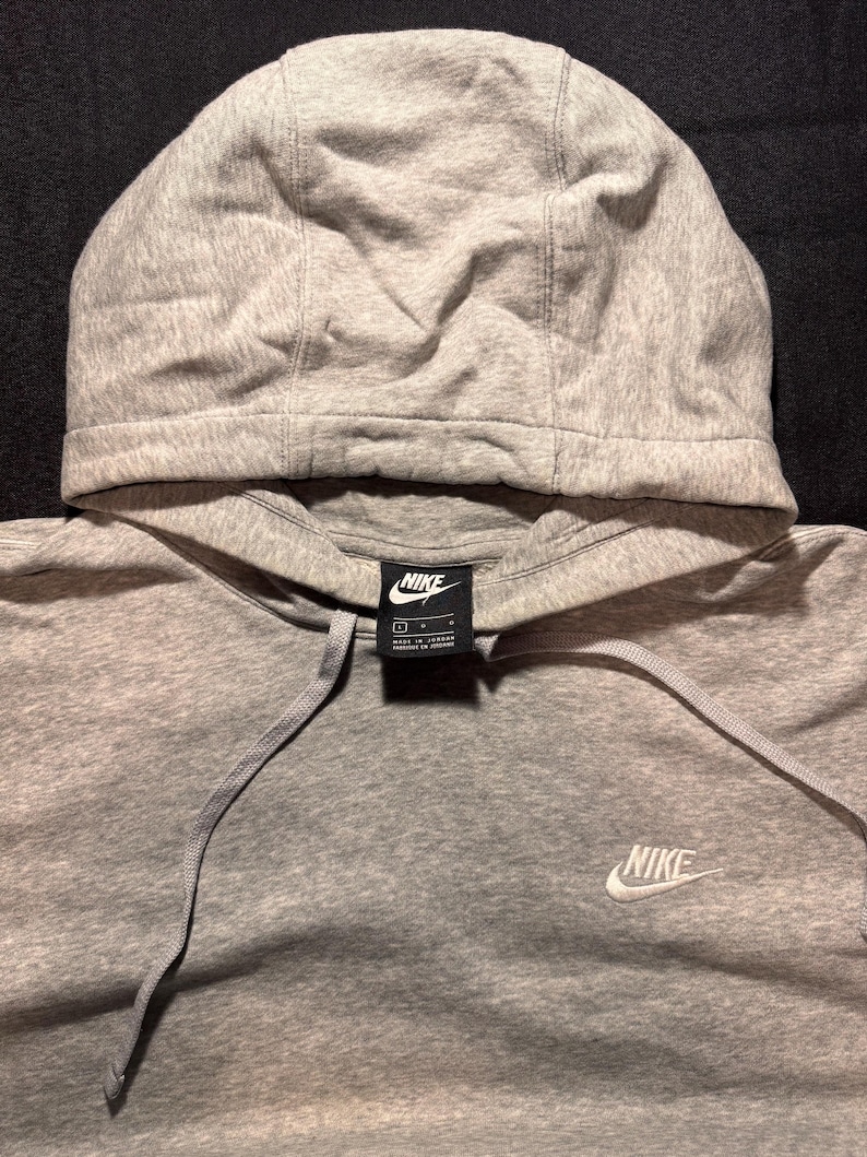 May include: A gray Nike hoodie with a drawstring and a hood. The Nike logo is visible on the chest and on a tag near the neckline. The hoodie is made of a soft, comfortable material.