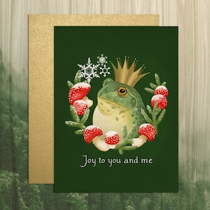 Illustrated portrait of a bullfrog, in tones of green and yellow, wearing a simple gold crown. The frog is encircled by a three quarters round wreath made of red amanita mushrooms, spruce sprigs, and snowflakes. Solid green background.