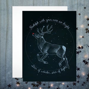 Background is dark night sky. There are stars in the sky. A reindeer constellation is traced out in light blue, with a bright red star at the nose tip. A circle of text says "Rudolph with your nose so bright, Star of wonder, star of light."